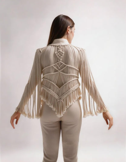 Espalda de mujer luciendo chaqueta artesanal de macramé ANASTASI color crema con flecos, combinada con pantalón beige, sobre fondo neutro.