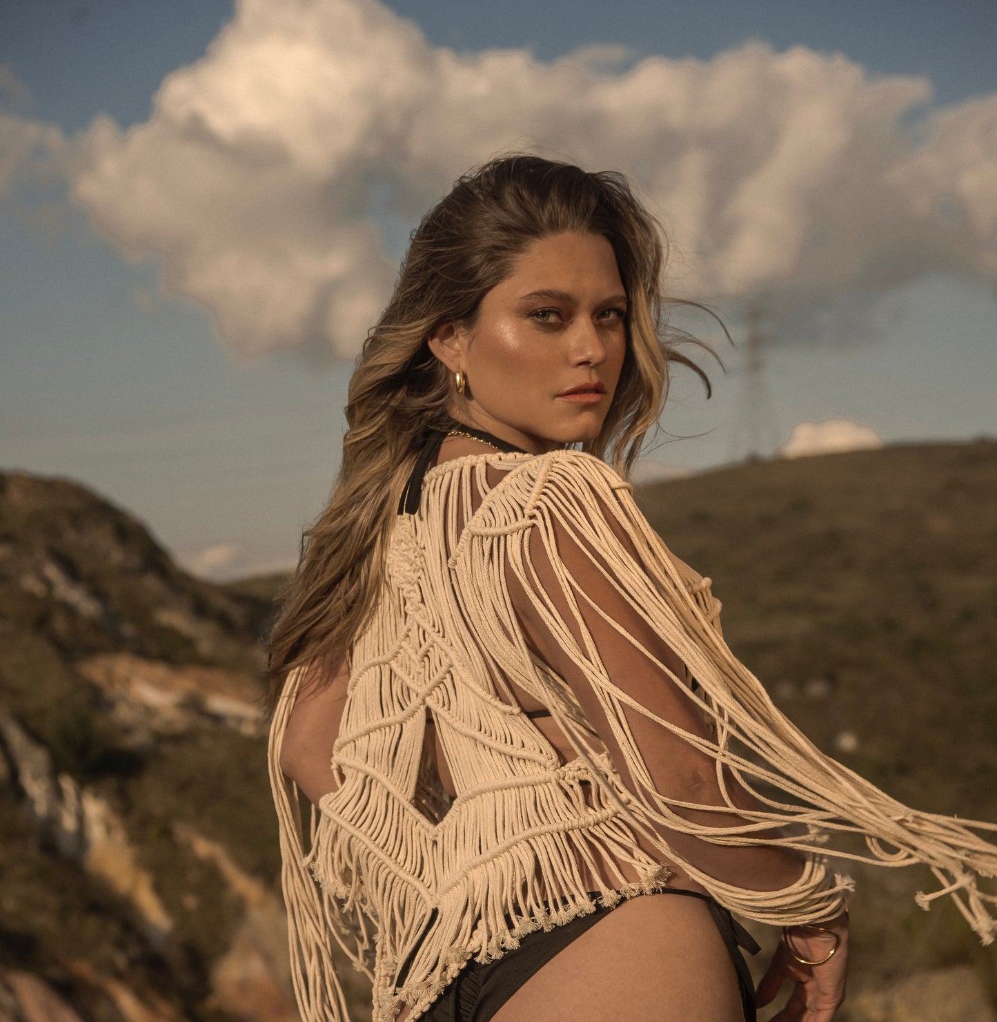 Mujer con chaqueta de macramé ANASTASI en entorno natural, estilo boho sofisticado, al atardecer.